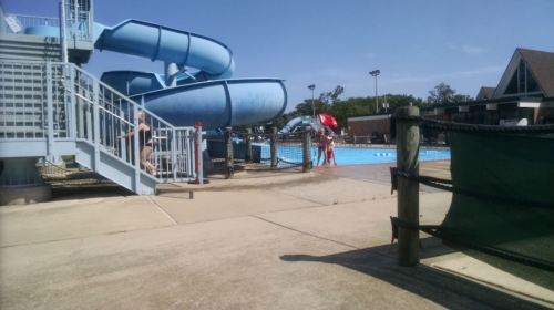 A swimming pool area featuring a large water slide, lifeguard, and people enjoying the sunny day.