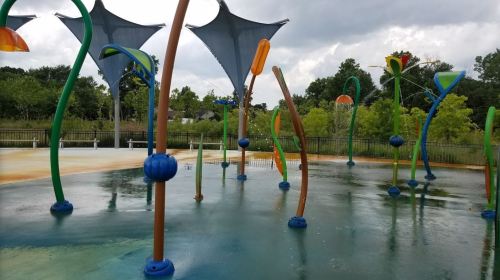 Colorful water play area with whimsical structures and canopies, surrounded by greenery under a cloudy sky.