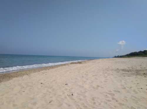 A serene beach scene with soft sand, gentle waves, and a clear blue sky in the background.