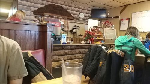 A cozy diner interior with wooden decor, a counter, and patrons seated at tables.
