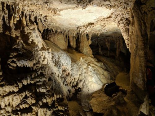 A dimly lit cave interior with stalactites and stalagmites, showcasing unique rock formations and textures.