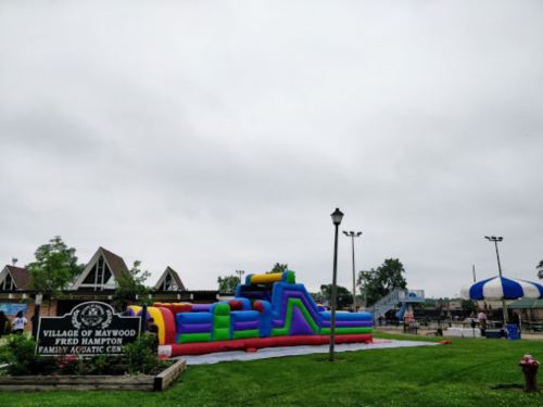 A colorful inflatable slide at a family aquatic center, with cloudy skies and a sign for the Village of Maywood.