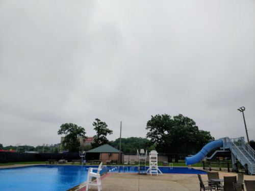 A cloudy day at an empty swimming pool with a slide and lounge chairs around the water.