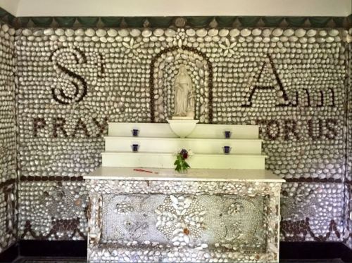 A decorative wall made of shells with a statue and altar, featuring the words "St. Francis" and "Pray for Us."