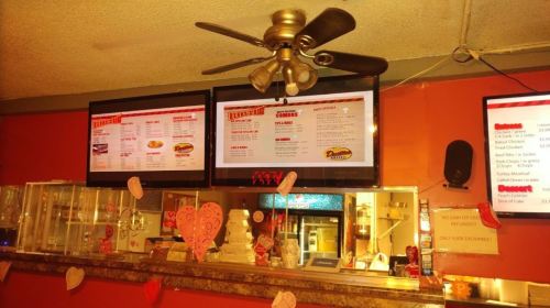 Menu boards displaying food options at a casual restaurant, with a ceiling fan and heart decorations in the background.