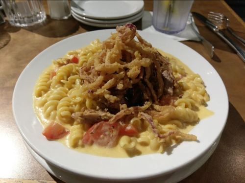 A plate of creamy pasta topped with pulled meat, diced tomatoes, and crispy fried onions.