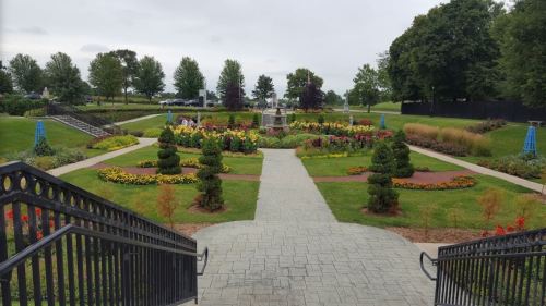 A landscaped garden with colorful flowers, neatly arranged paths, and greenery, viewed from a staircase.