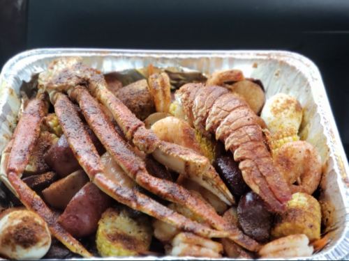 A tray of seasoned seafood, including crab legs, shrimp, and potatoes, ready to be served.