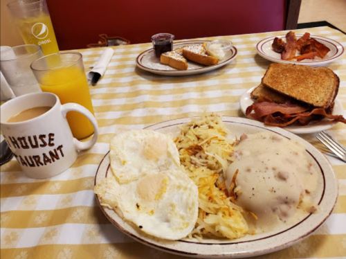 A breakfast plate with eggs, hash browns, sausage gravy, toast, bacon, and a mug of coffee, with orange juice in the background.