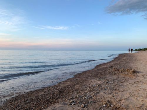 A serene beach at sunset with gentle waves and two people walking along the shore.