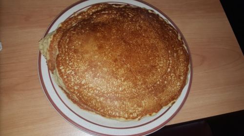 A stack of golden-brown pancakes on a plate, resting on a wooden table.