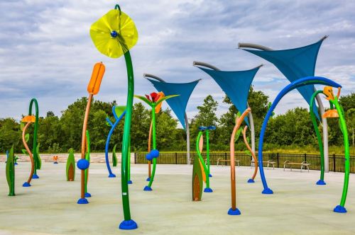 Colorful playground structures resembling flowers and plants under blue canopies, set in a green park.
