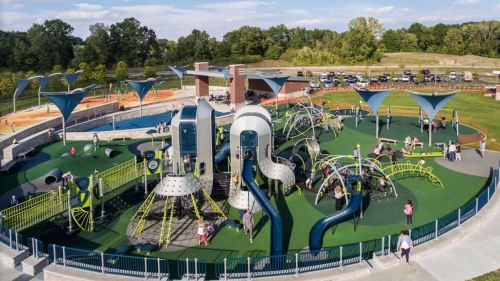 Aerial view of a vibrant playground with various climbing structures, slides, and children playing in a green park setting.