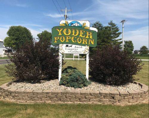 Sign for Yoder Popcorn featuring colorful graphics and the text "Amish Country Goodness," surrounded by landscaping.