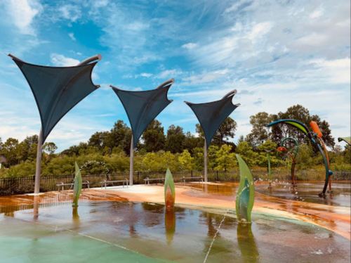 A colorful splash pad with large, sail-like canopies and playful water features under a blue sky.