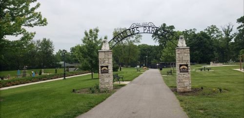 Entrance to Phillips Park, featuring a stone archway and a pathway lined with greenery and benches.