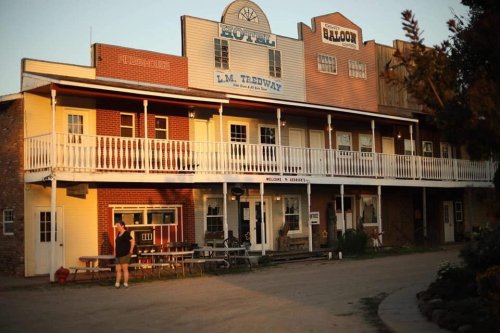 Historic building with a hotel and saloon, featuring a porch and outdoor seating in a rustic setting.