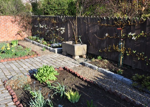 A well-maintained garden with flower beds, a stone path, and a wooden fence, featuring blooming plants and greenery.