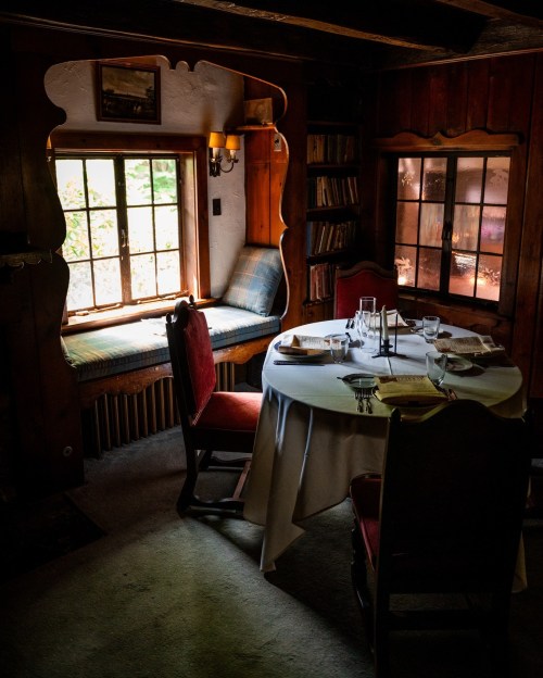Cozy dining area with a round table, red chairs, and a window seat, surrounded by wooden walls and shelves.