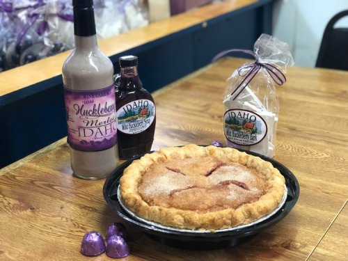A huckleberry pie on a wooden table, accompanied by huckleberry syrup and a bottle of huckleberry wine.