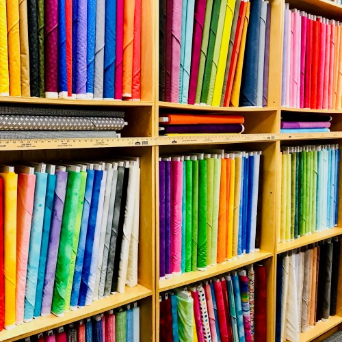 A colorful display of neatly rolled fabrics arranged on wooden shelves, showcasing a variety of patterns and colors.