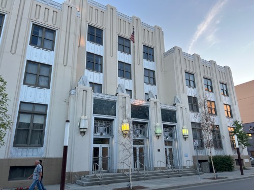 Art Deco-style building with large entrance, decorative details, and a person walking by on the sidewalk.