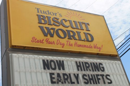 Sign for Tudor's Biscuit World announcing "Now Hiring Early Shifts" with a bright yellow background.
