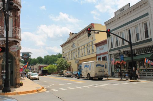 A quaint street scene featuring historic buildings, parked cars, and traffic lights under a partly cloudy sky.
