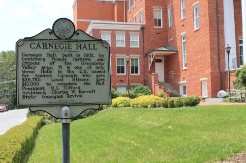 Sign for Carnegie Hall, built in 1902, with a brick building in the background, detailing its history and architectural style.