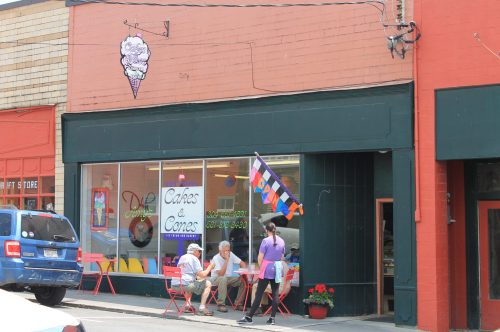 A colorful ice cream shop with outdoor seating, featuring a sign for "Cakes & Cones" and a person serving customers.