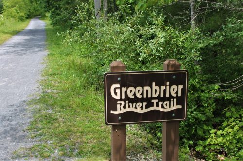 Sign for Greenbrier River Trail beside a gravel path surrounded by greenery.