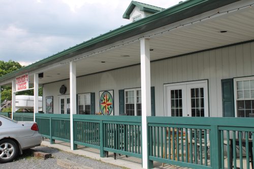 A building with a green porch, white walls, and decorative windows, featuring a colorful star design on the side.
