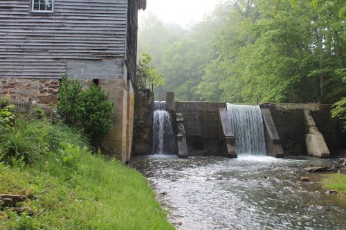 A serene scene of a watermill beside a stream, featuring two small waterfalls and lush green surroundings.