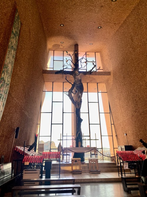 Interior of a church featuring a large wooden crucifix and tall windows, with benches and candles in the foreground.