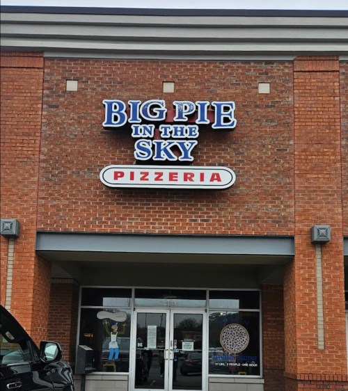 Sign for "Big Pie in the Sky Pizzeria" on a brick building, featuring a cartoon pizza character in the window.