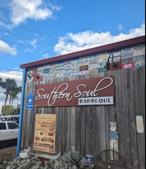 Sign for Southern Soul Barbeque on a wooden wall, adorned with various license plates and a blue sky above.