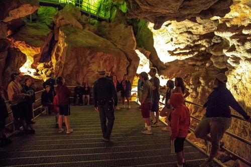 A guided tour group explores a lit cave, surrounded by rocky formations and metal walkways.
