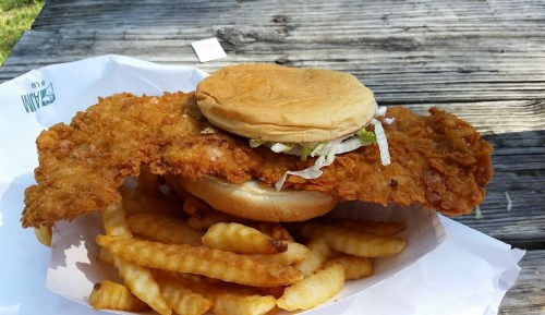 A large fried chicken sandwich with lettuce on a bun, served with crinkle-cut fries on a wooden table.