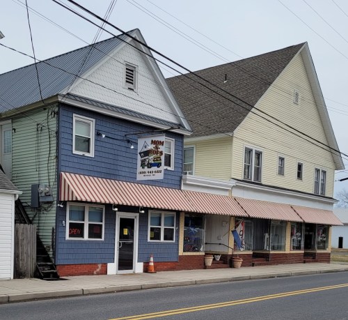 A blue building with a sign reading "Mom's" and a yellow building next door, both with striped awnings.