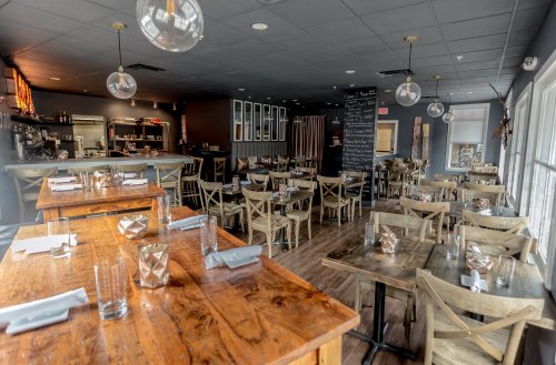 A cozy restaurant interior with wooden tables, chairs, and a chalkboard menu, featuring warm lighting and a welcoming atmosphere.