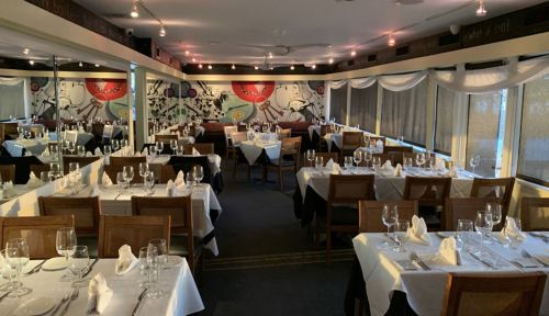 A dining room with neatly set tables, white tablecloths, and colorful wall art, creating an inviting atmosphere.