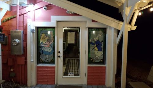 A colorful entrance with stained glass depicting Alice and the White Rabbit, framed by a white porch.