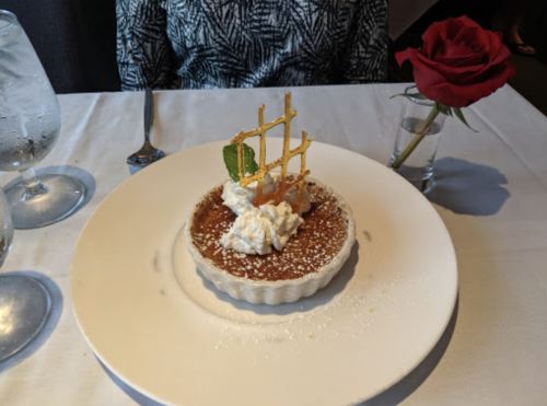A dessert with a caramelized top, whipped cream, and a decorative sugar lattice, accompanied by a rose on the table.
