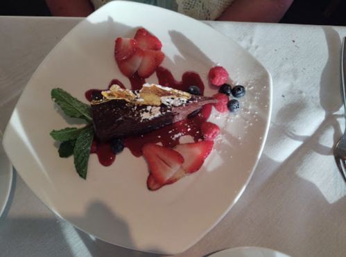 A slice of chocolate cake garnished with berries, mint, and a drizzle of sauce on a white plate.