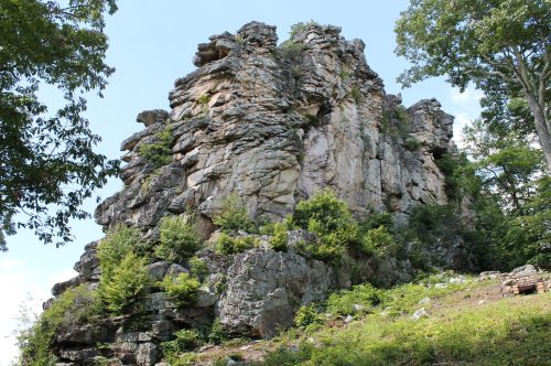 A large rock formation surrounded by greenery under a clear blue sky.
