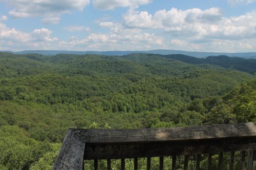 A scenic view of lush green mountains under a partly cloudy sky, seen from a wooden overlook.