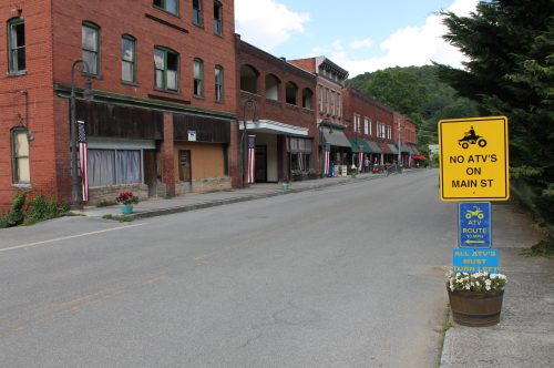A quiet Main Street lined with brick buildings and signs, including one prohibiting ATVs and another indicating an ATV route.