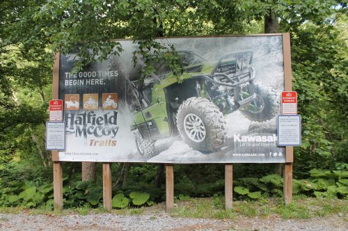 Billboard promoting Hatfield McCoy Trails with an off-road vehicle, surrounded by trees and a gravel path.
