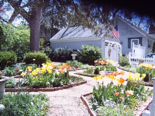 A charming house with a blue exterior surrounded by vibrant flower beds and a small American flag.