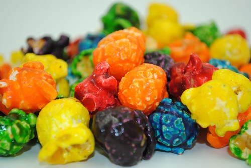 A colorful assortment of popcorn kernels in various bright hues, including orange, yellow, green, red, and purple.